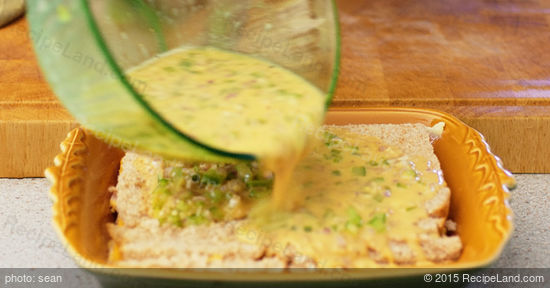 Pouring egg mixture over breakfast casserole layers