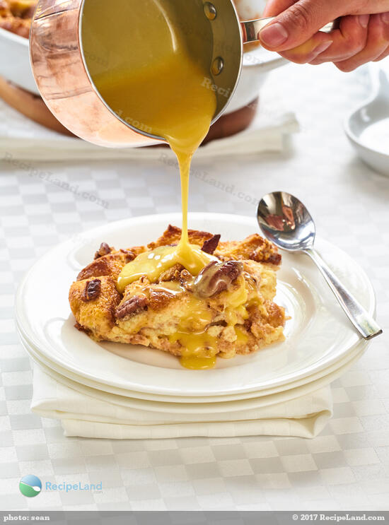 Pouring whiskey sauce for bread pudding over a serving of Lazarus bread pudding.