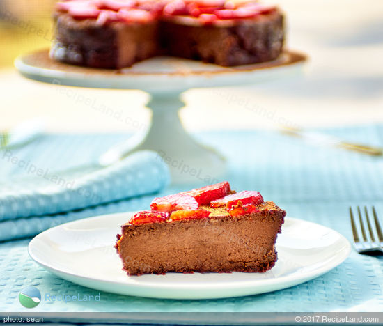 A slice of flourless chocolate cake topped with strawberries backlit by sunlight