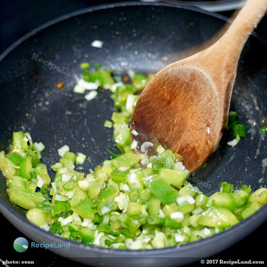 Stirring diced green bell pepper and scallions to combine