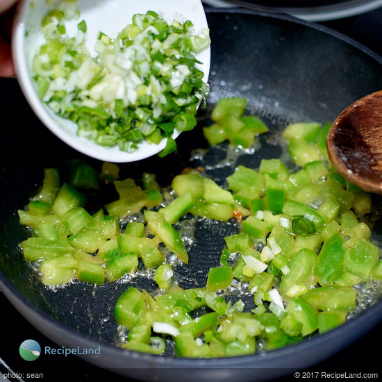 Adding scallions to a skillet of green bell pepper.