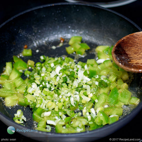 Scallions and diced green bell peppers in a skillet