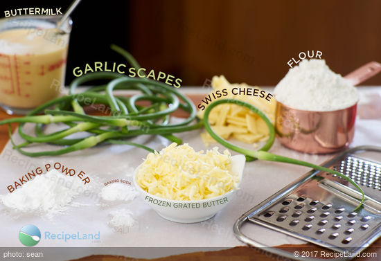Ingredients to make garlic scape cheese biscuits on a wood cutting board