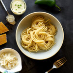 Freshly cooked spaghetti arranged in a bowl with Jalapeno pepper cream sauce and parmesan shavings on the side.