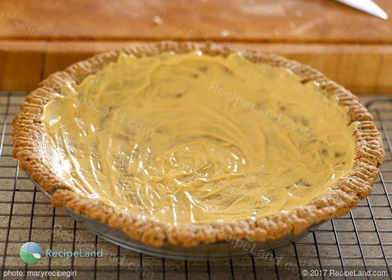 Blind baked herbed pie crust spread with Dijon mustard ready for filling in a glass pie plate on a wire rack.