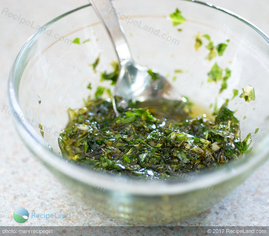 Prepared herb drizzle for topping herbed tomato pie. Herbs and garlic mixed with olive oil in a glass <a href=