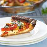 A juicy slice of Cheesy Herbed Fresh Heirloom Tomato Pie on a white plate with whole pie in the background and serving fork off to the side.