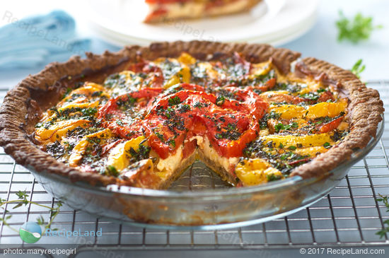 Close-up showing the layers of a cheesy herbed fresh heirloom tomato pie in a glass pie plate on a wire rack surrounding be fresh thyme.