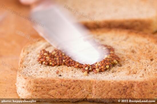 Spread the mustard evenly over one slice of toasted bread with a serving knife.