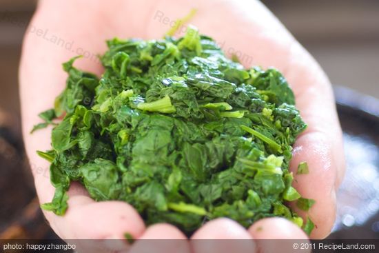 With the back of a spatula, gently press the spinach to release excess water.