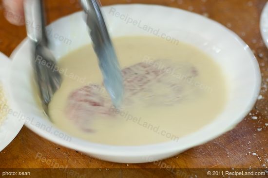 With a tongs, dip the chop into the milk mixture,
