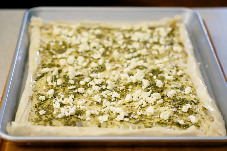 Sprinkle about half of the crumbled feta cheese over the pesto layer.