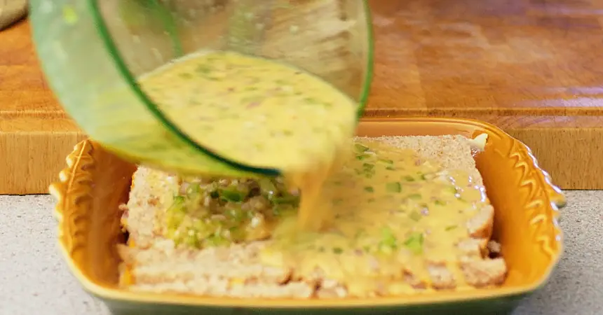 Pouring egg mixture over breakfast casserole layers