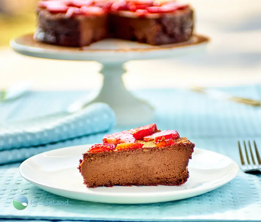 A slice of flourless chocolate cake topped with strawberries backlit by sunlight