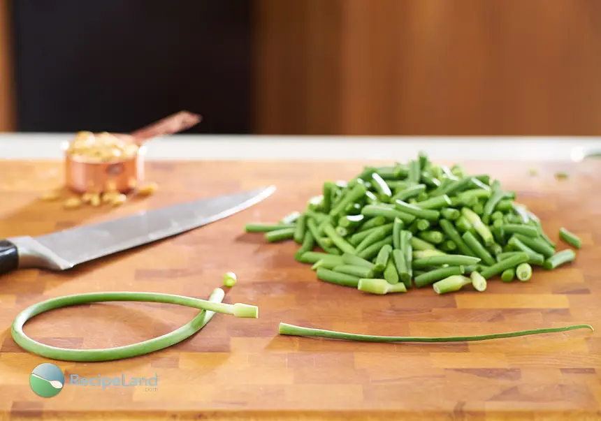 Prepared garlic scapes; trimemed and chopped on a wood cutting board with a chef’s knife and pine nuts. z To prepare garlic scapes; trim off the tough top above the bulbous tip and trip the bottom.