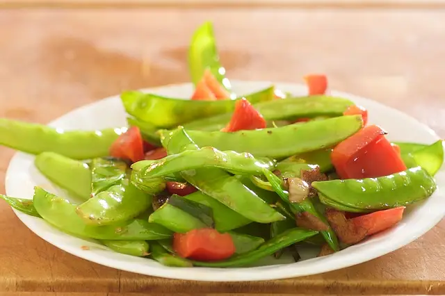 Add the snow peas, red bell pepper and garlic to a hot skillet with 1 tablespoon of vegetable oil added,