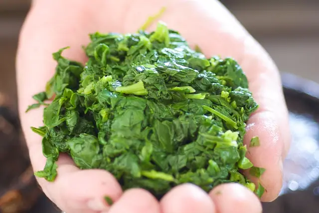 With the back of a spatula, gently press the spinach to release excess water.