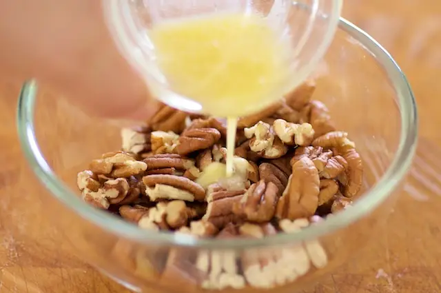 In a medium bowl, pour the melted butter into the coarsely chopped pecans.