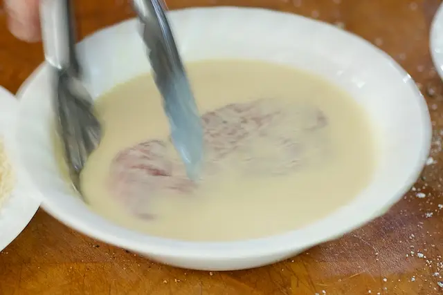 With a tongs, dip the chop into the milk mixture,